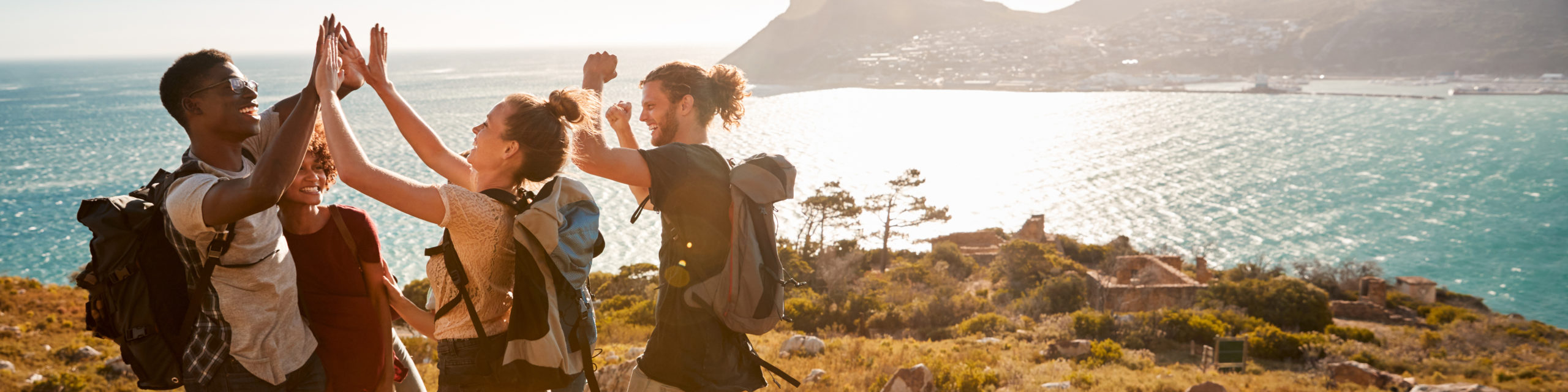 Young adult friends on a hike celebrate reaching a summit near the coast, full length, side view